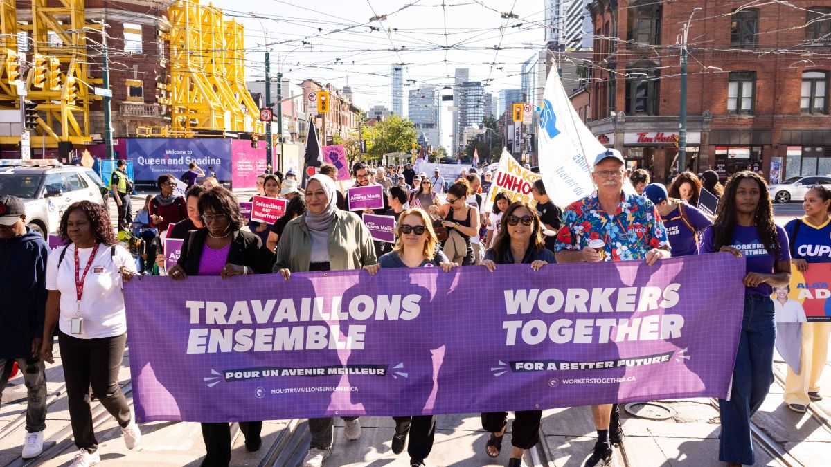 Des personnes brandissant une bannière « Workers Together – Travailleurs Ensemble » lors d'un défilé de la Fête du Travail. Person holding a Workers Together rally sign that reads, "Hands off our right to strike"
